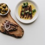 Delicious arrangement of anchovies and olives on a wooden board. Perfect food photography for culinary topics.