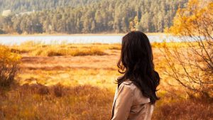 Woman in autumn landscape looking at serene lake, surrounded by colorful fall foliage.
